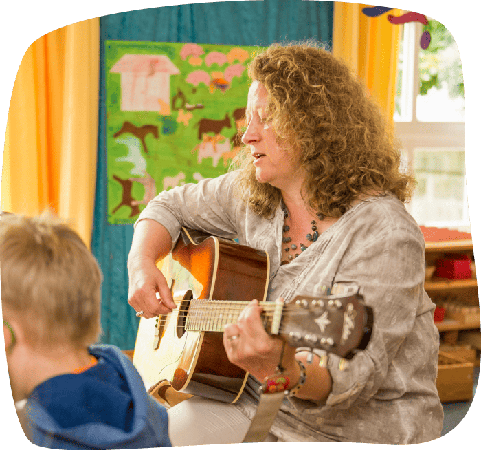 Erzieherin spielt Gitarre für Kinder im Gruppenraum des Integrativen Montessori Kindergartens Bayreuth