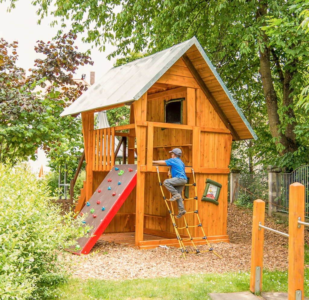 Holzspielhaus mit Kletterleiter und roter Rutsche im Garten des Integrativen Montessori Kindergartens Bayreuth