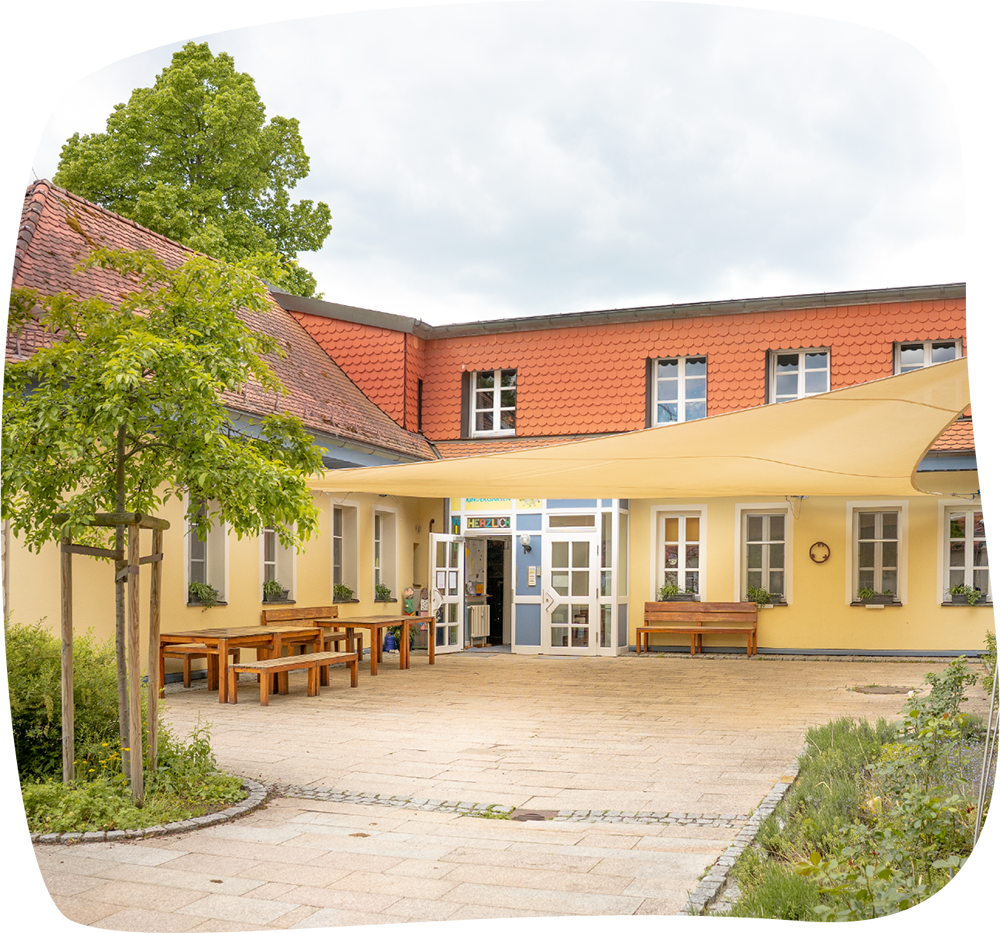 Innenhof des Integrativen Montessori Kindergartens Bayreuth mit Eingangsterrasse, Sonnensegel und Bäumen