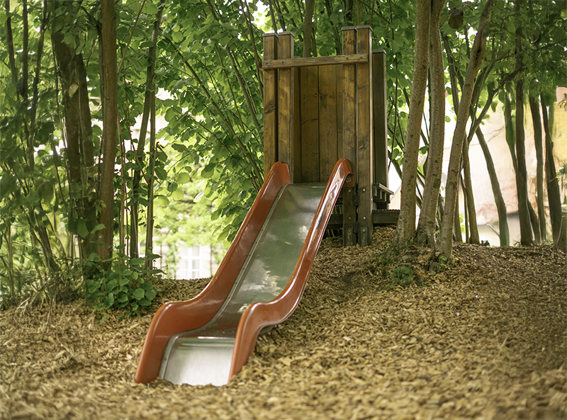 Rote Rutsche zwischen Bäumen im naturnahen Garten des Integrativen Montessori Kindergartens Bayreuth